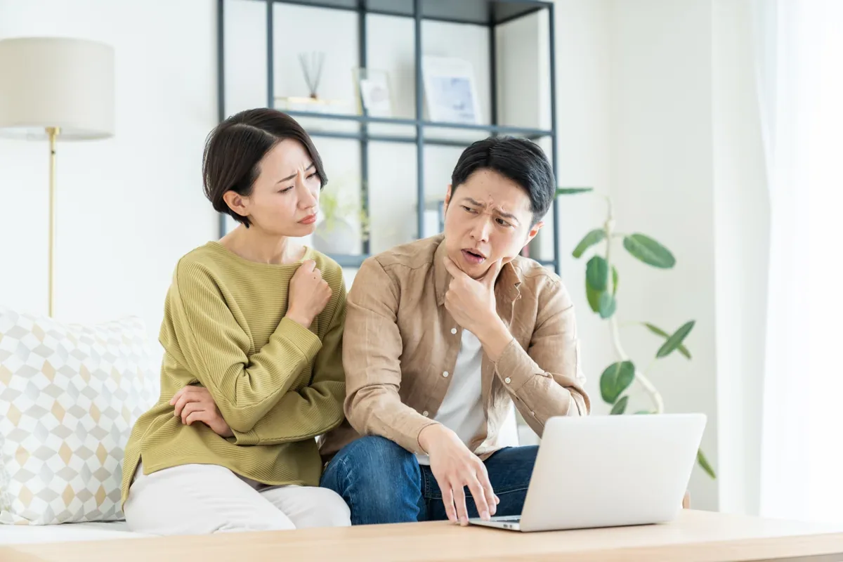 リビングでノートパソコンの画面を確認する夫婦