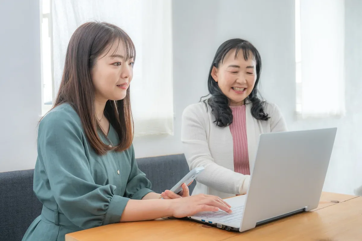 自宅でパソコン画面を見ながら相談する二人の女性