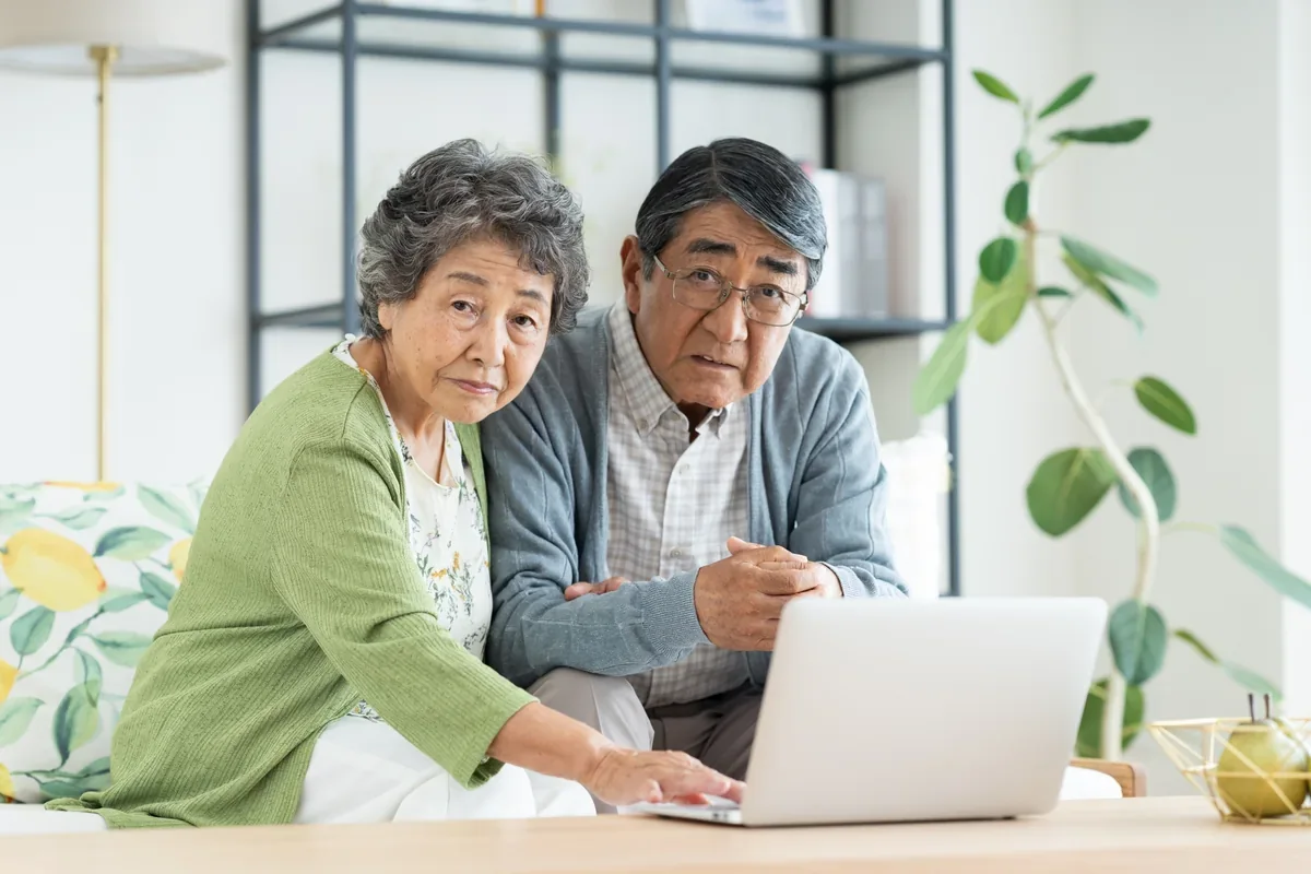 自宅でパソコン画面を見ながら悩むシニア夫婦