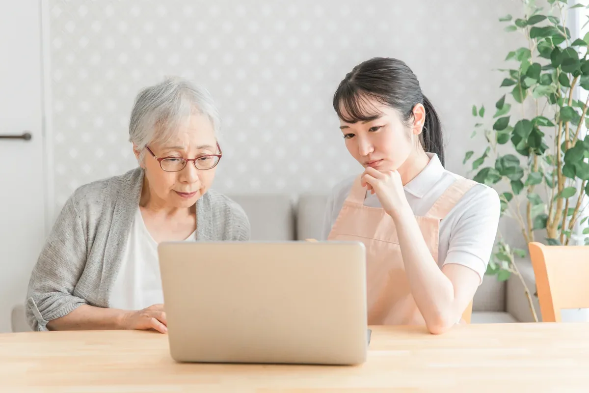 自宅でシニア女性のパソコン操作を支える女性