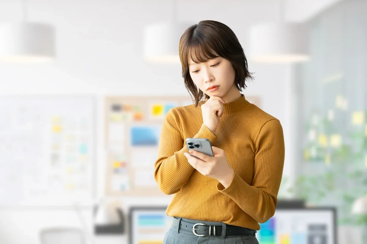 自宅でスマートフォンを見ながら考える女性
