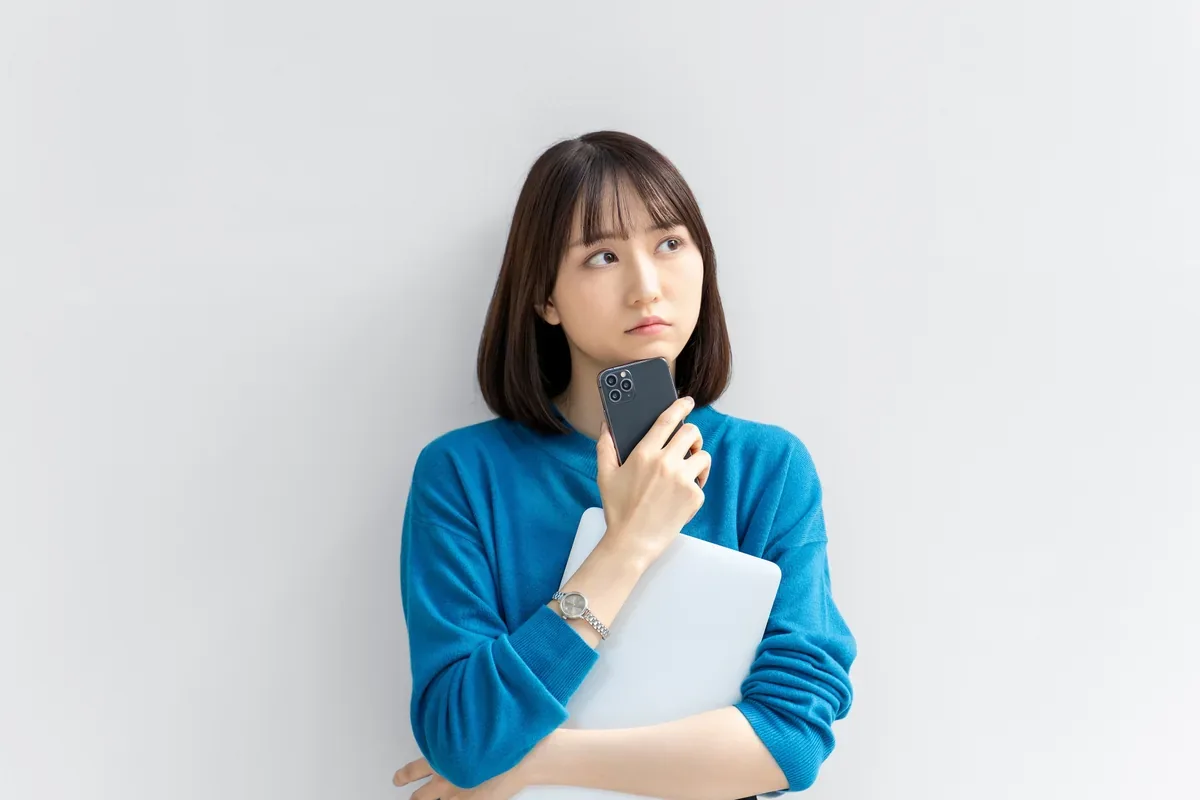 スマートフォンとノートパソコンを前に考える女性